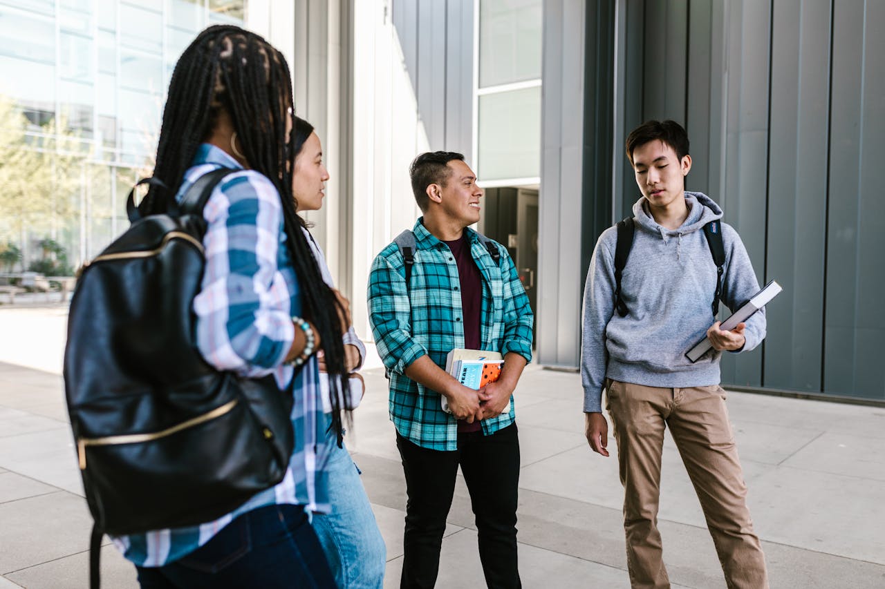 A group of university students socializing and holding books outside on campus.