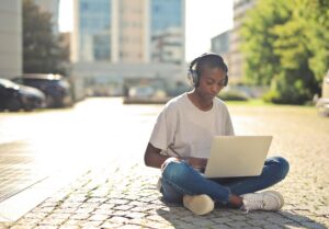 Young woman sitting outdoors, using a laptop for online learning on a sunny day.